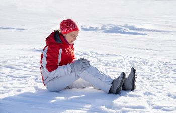 Woman with knee pain sitting on the snowy ground.